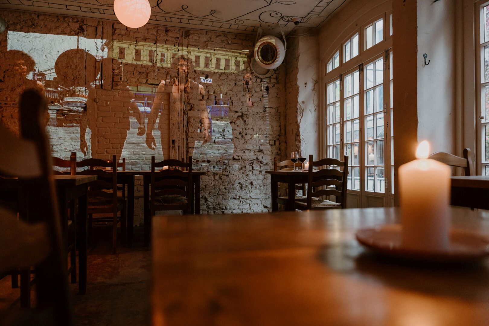 Fett ist eine Weinbar in Düsseldorf, man sieht das unverputzte Mauerwerk, auf dem ein Film aus den 70er Jahren ohne Ton projiziert wird. Außerdem viel Tische und Stühle aus Holz.