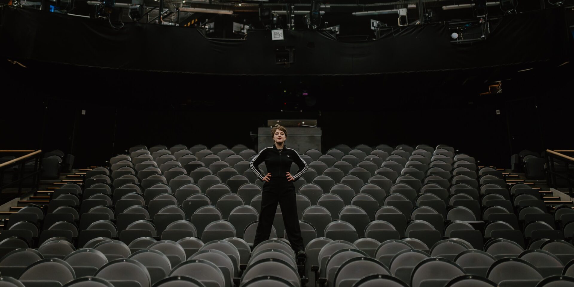 Sophie Stockinger steht breitbeinig in einem schwarzen Trainingsanzug zwischen den leeren Zuschauerreihen im Düsseldorfer Schauspielhaus.