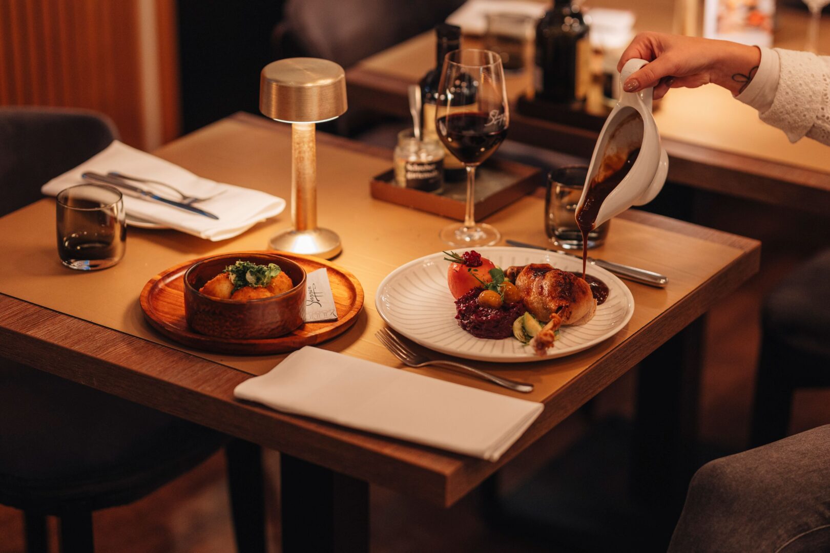 Man sieht einen gedeckten Holztisch mit einer Gänsekeule, eine Hand im Bild hält die Sauciere und gießt Soße auf die Keule. Das Stappen zählt zu den Restaurants in Düsseldorf.