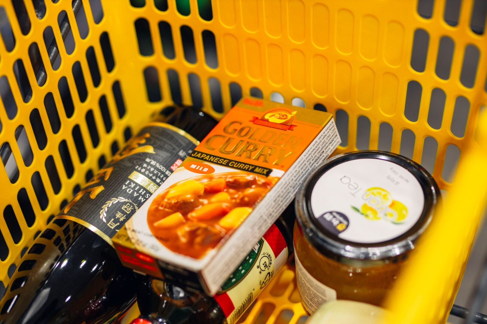 Man sieht einen gelborangen Supermarkteinkaufskorb im Anschnitt, darin ist unter anderem eine Packung Golden Curry.