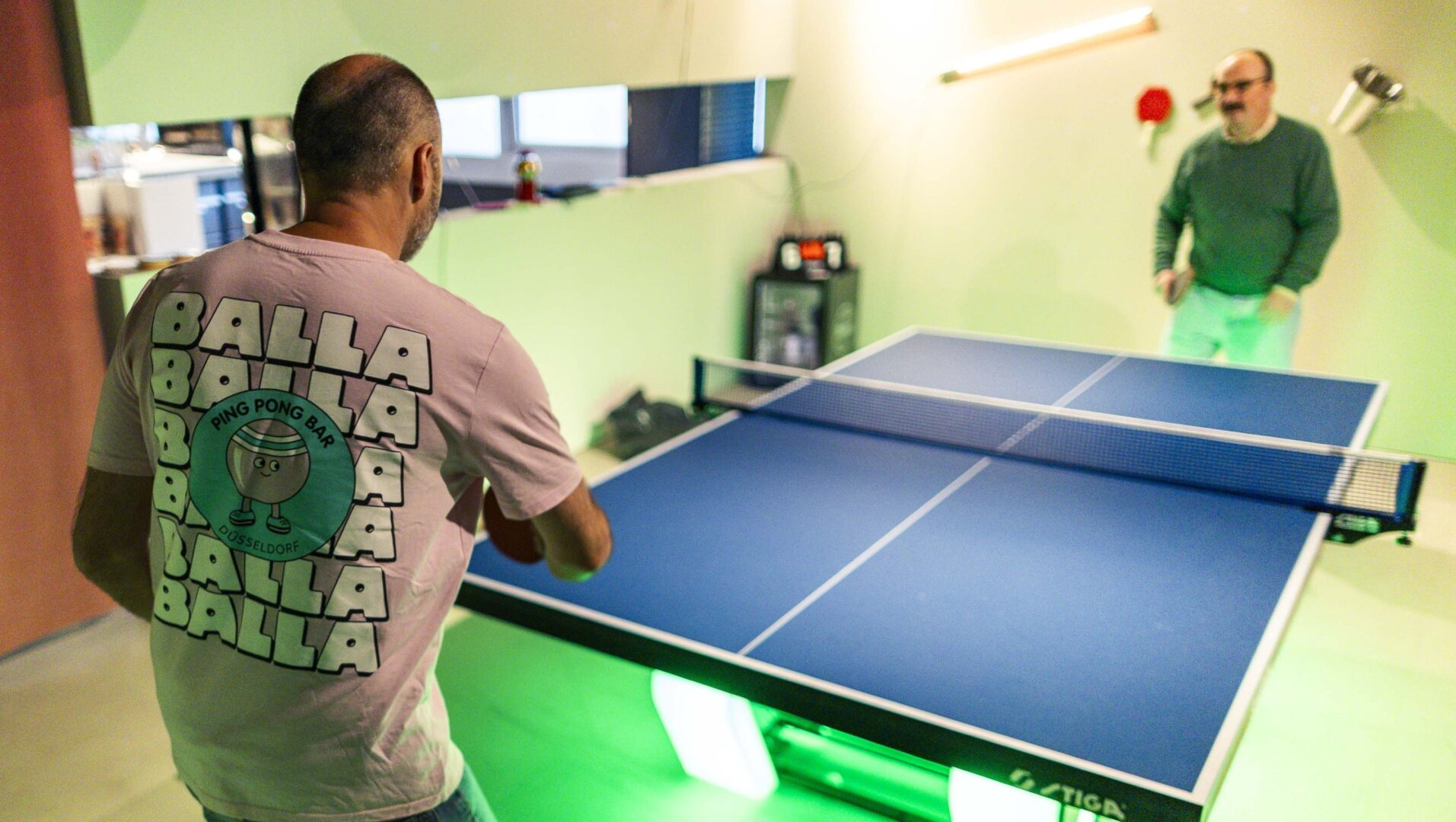 Alain Bieber spielt gegen Autor Clemens Henle Tischtennis, er trägt ein T-Shirt mit Balla Balla Aufdruck.