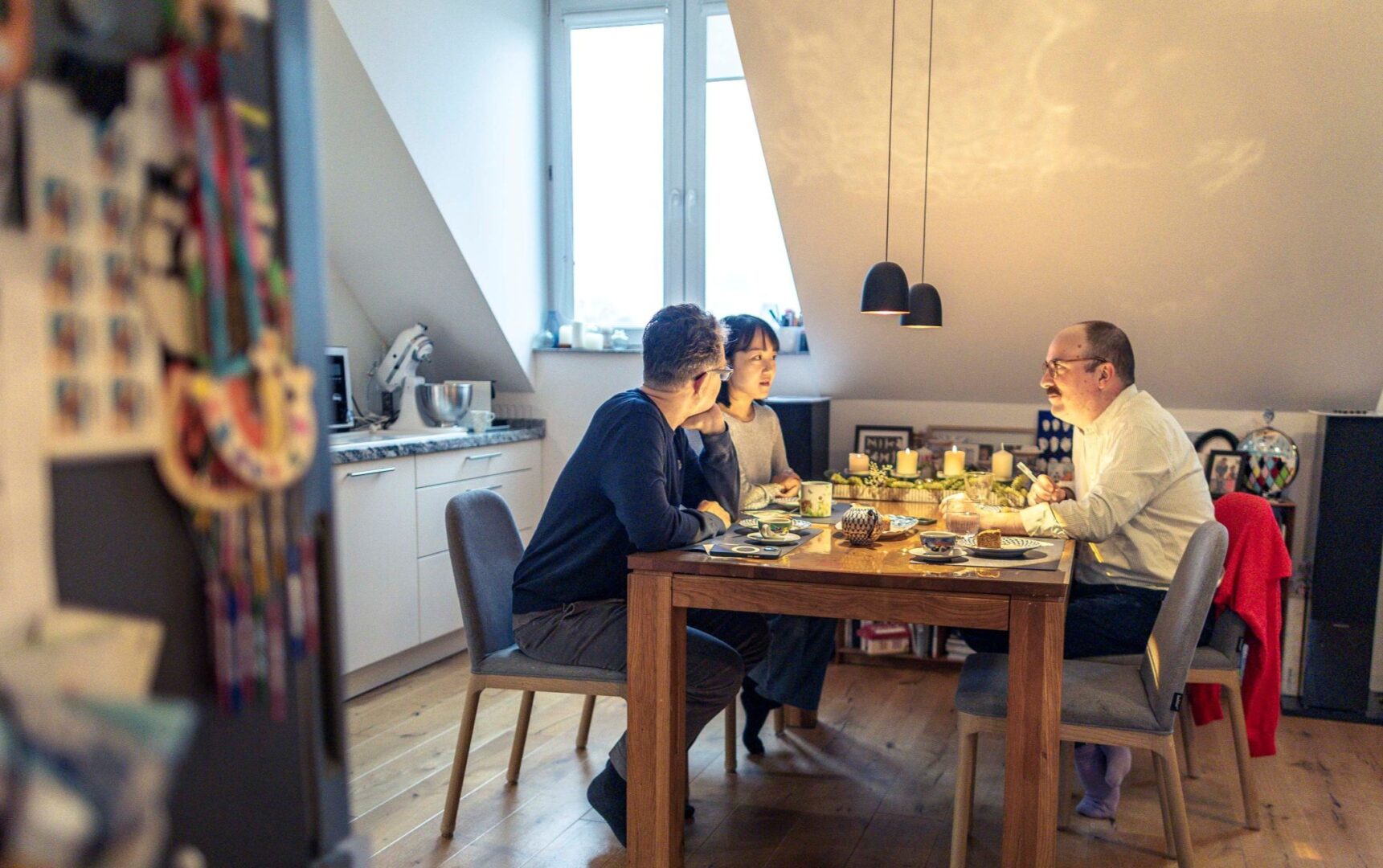Man sieht Clemens Henle (re) mit Fukaba und Yurie am Küchentisch mit Adventsgesteck und in weihnachtlicher Atmosphäre im Interview.