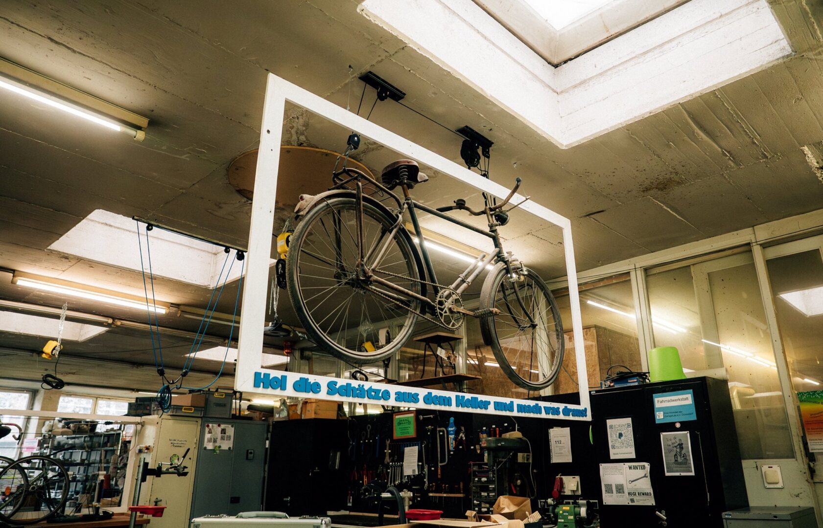 Man sieht ein Fahrrad von der Decke hängen, das in einem Rahmen steckt. Unten im Rahmen steht: Hol die Schätze aus dem Keller und mach was draus!