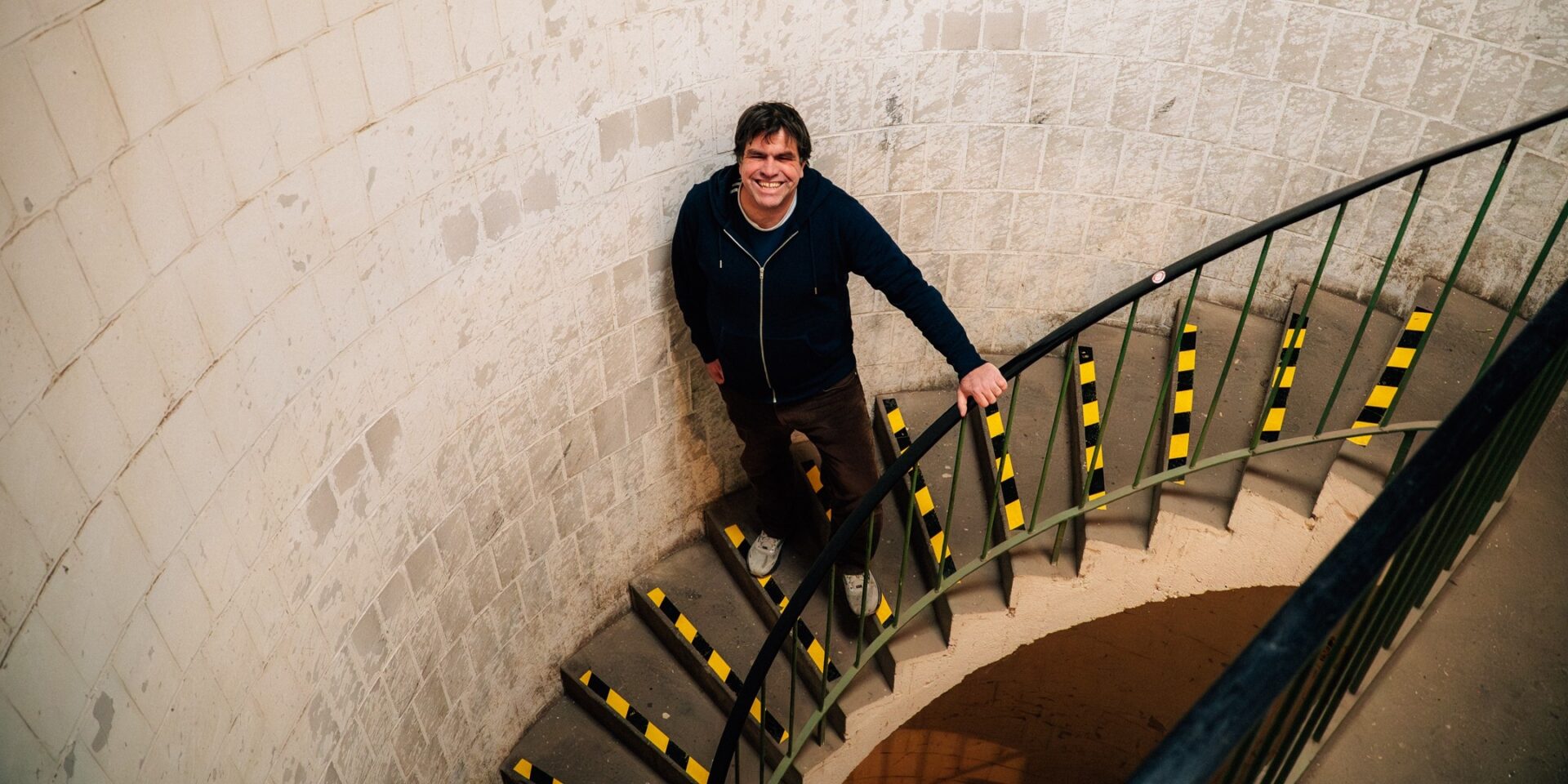 Markus Lezaun, Geschäftsführer Maschinendorf, steht auf einer Wendeltreppe im Coworkingspace und schaut nach oben in die Kamera.