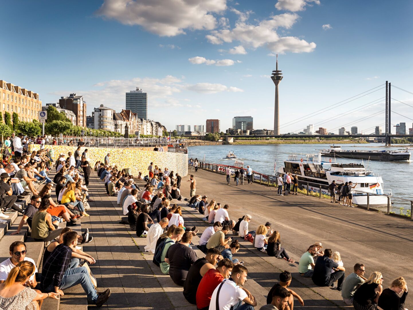 Sommer am Rhein. Man sieht viele Menschen auf der Freitreppe vor dem Schifffahrtmuseum Düsseldorf sitzen.