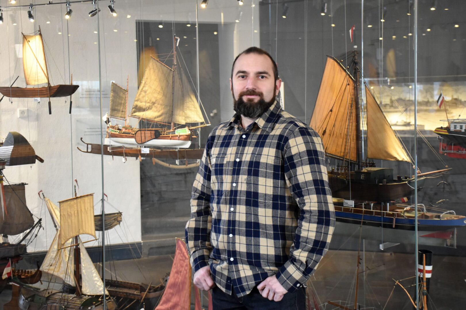 Markus Todoric, Leiter Schifffahrtmuseum Düsseldorf, im Portrait vor einer Vitrine mit Modellen diverser Segelschiffe.
