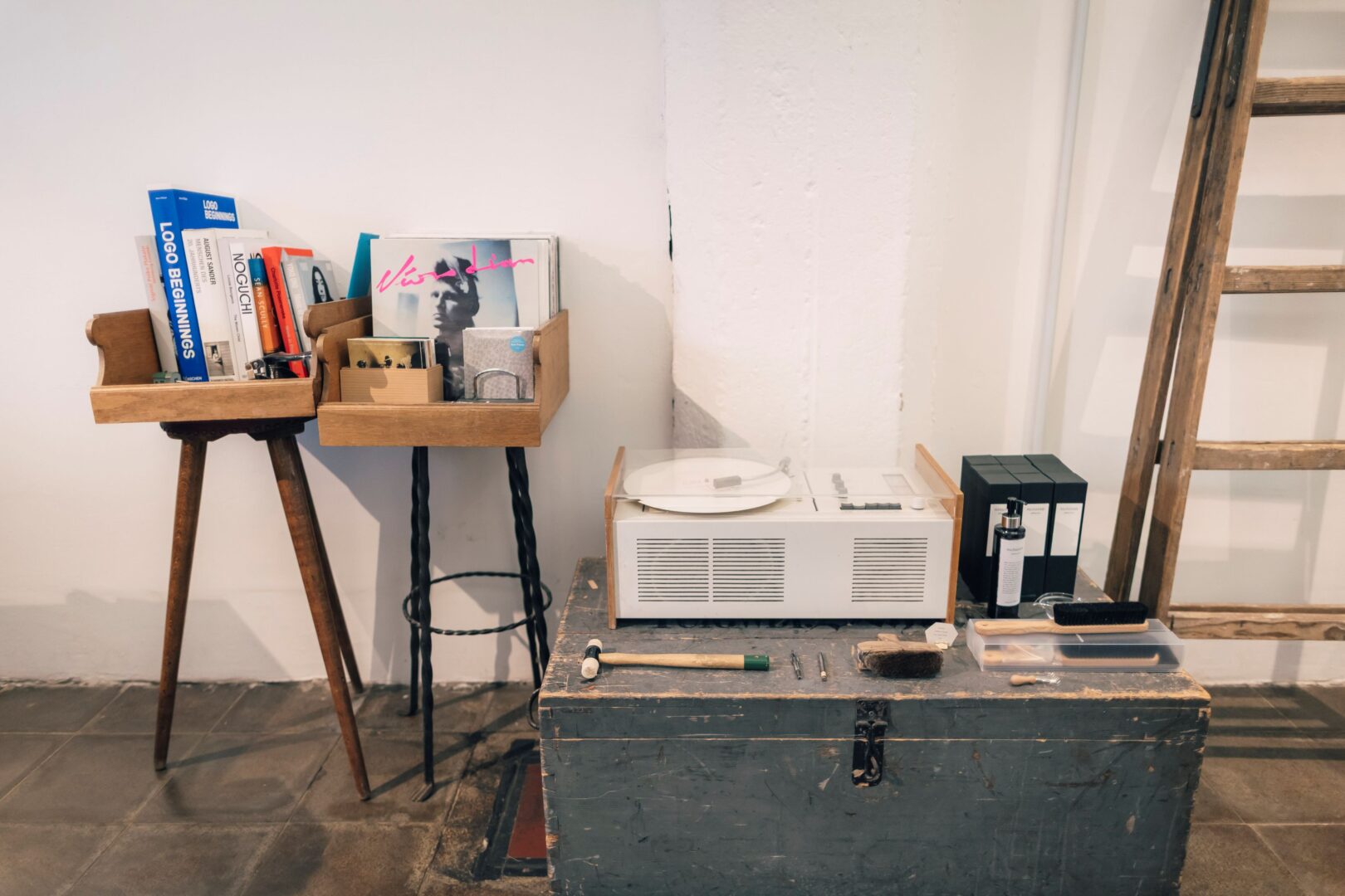 Im Atelier von Suzusan steht ein Plattenspieler von Dieter Rams, der Schneewittchensarg, rechts daneben eine alte Holzleiter, links daneben zwei Barhocker, auf denen jeweils ein Tablett mit ausgewählten Büchern und Platten stehen. 