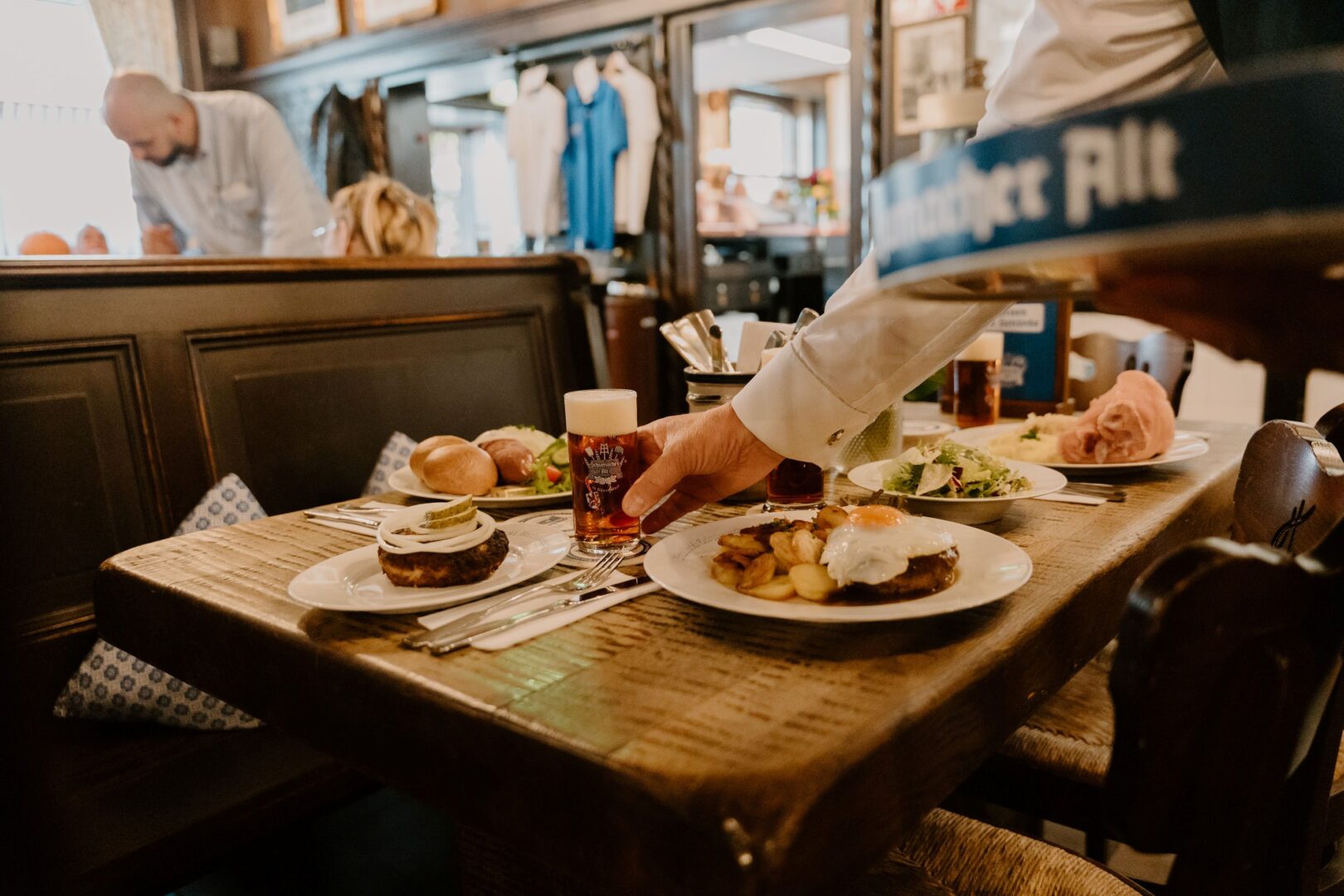 Man sieht einen Gastraum in dem Brauhaus Düsseldorf Schumacher. Man sieht einen gedeckten Tisch mit verschiedenen Spezialitäten wie Eisbein, Frikadelle mit Zwiebelnringen und Gürkchen und Röggelchen mit Blutwurst.