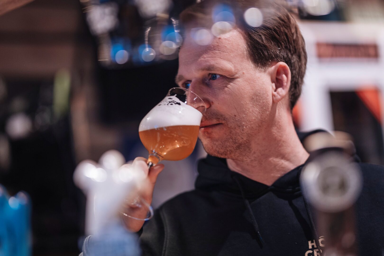 Sebastian hält ein Glas mit hellem Bier dicht an die Nase und riecht daran. 