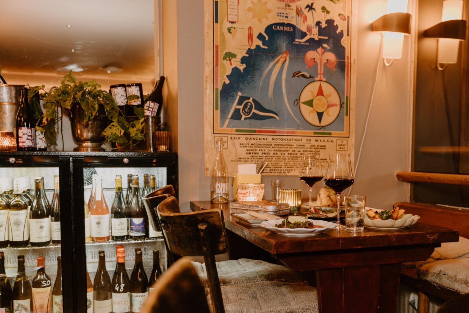 Im Janot's Bar Bistrot sieht man einen Tisch am Fenster, der eingedeckt ist und links daneben Weinkühlschränke, die gefüllt sind.