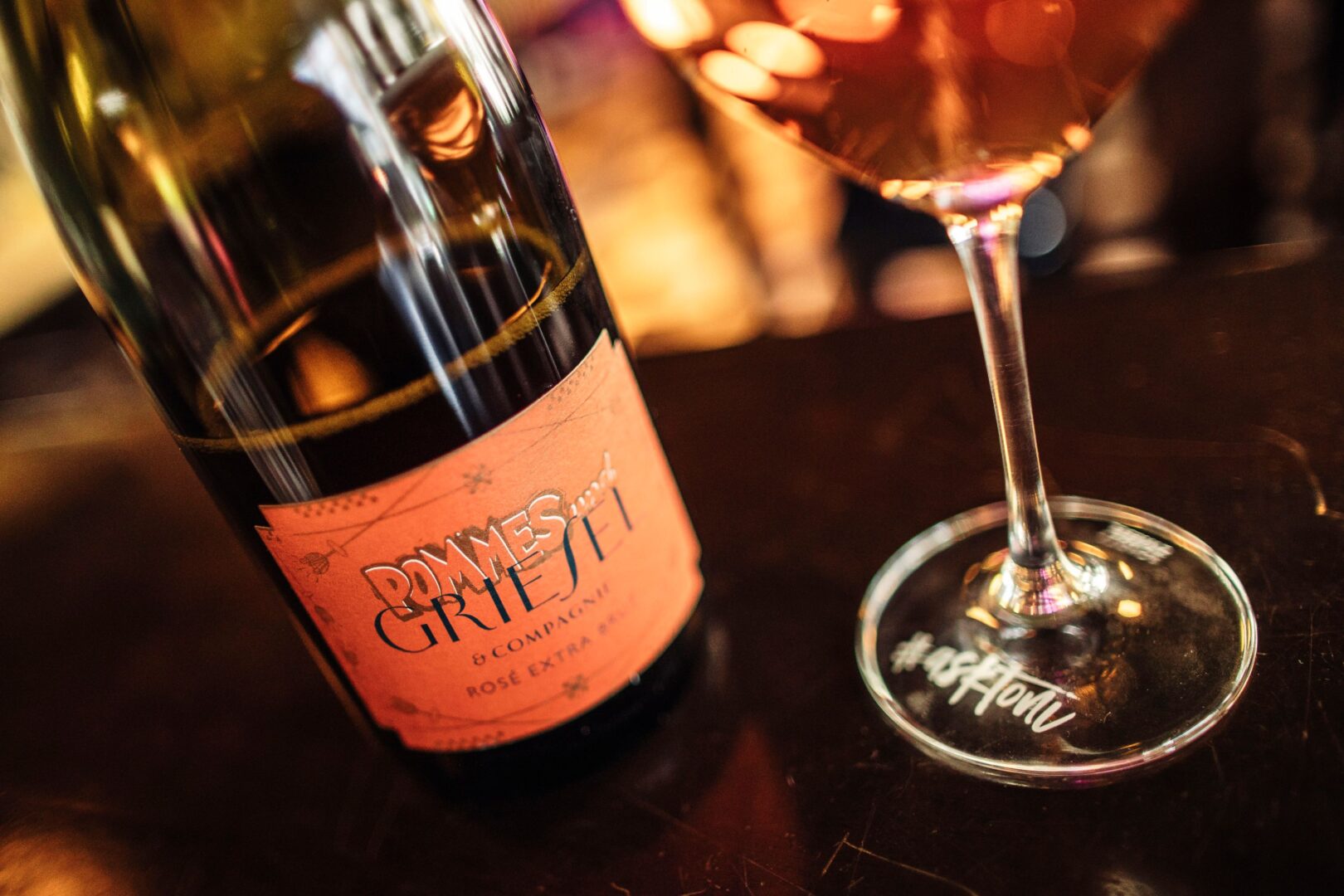 Man sieht eine Flasche Wein und ein Glas. Das Weinetikett zeigt, dass es eine Kooperation von Pommes und Wein mit einem Winzer ist. 