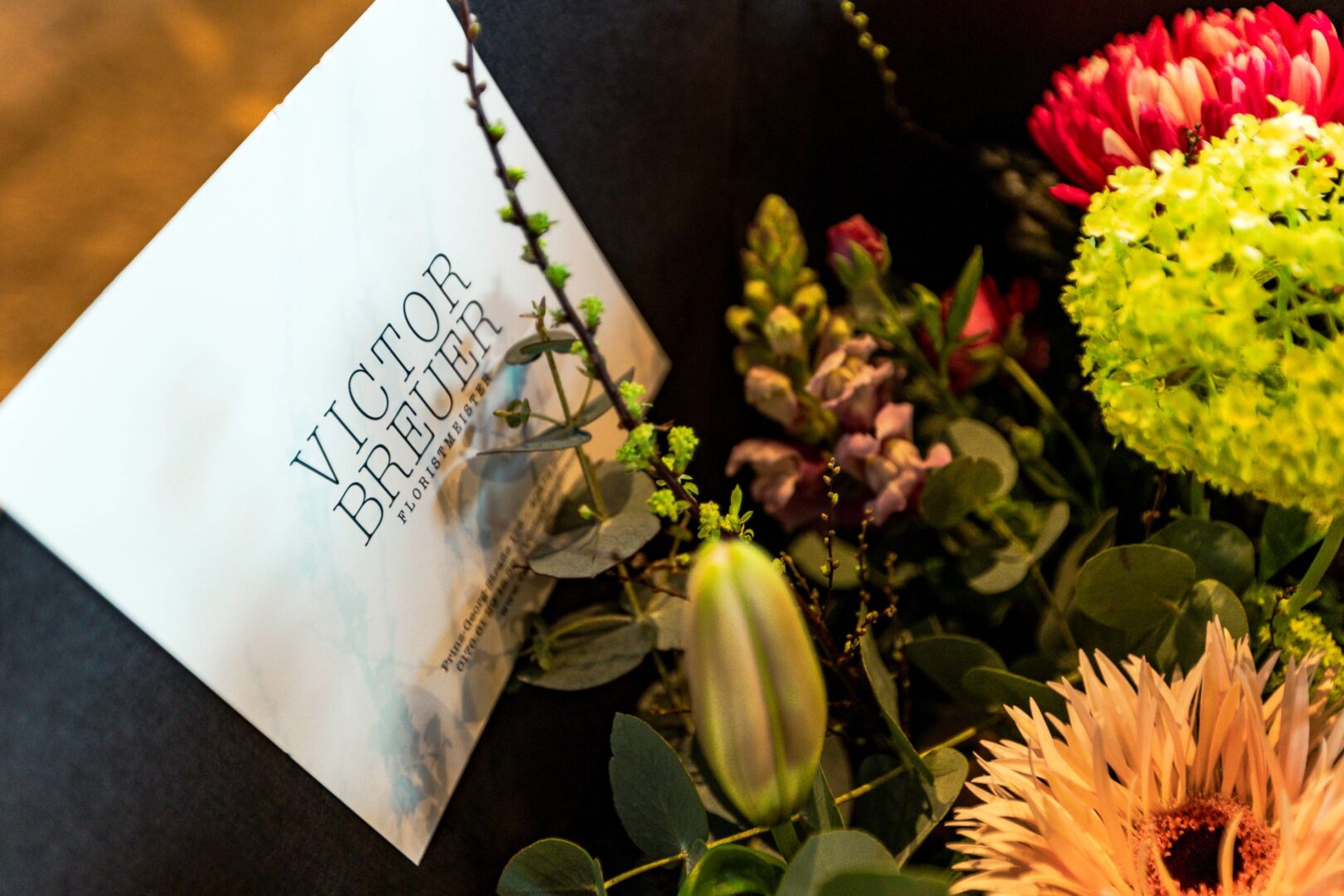 Ausschnitt eines Blumengestecks mit einer großen Karte, auf der Victor Breuer steht.