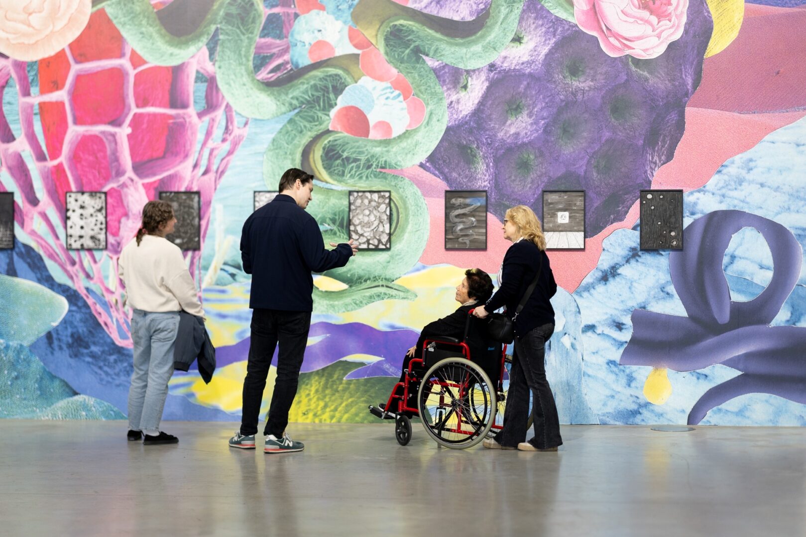 Vier Menschen vor einem Wand-füllenden Gemälde in der Sammlung Philara. Eine Person sitzt im Rollstuhl und wir von einer Frau geschoben. 