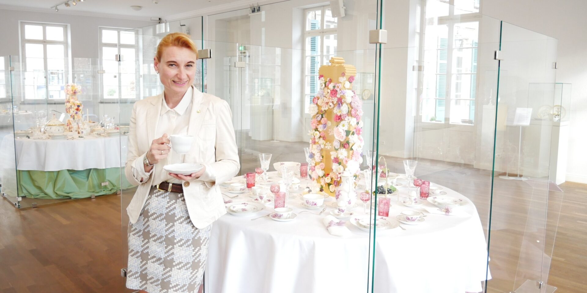 Dr. Daniela Antonin Aeberli, Leiterin des Hetjens Museum, steht mit einer Porzellantasse vor einer Vitrine, in der ein gedeckter Tisch mit wertvollem Porzellan "Copenhagen Royal" gedeckt ist.
