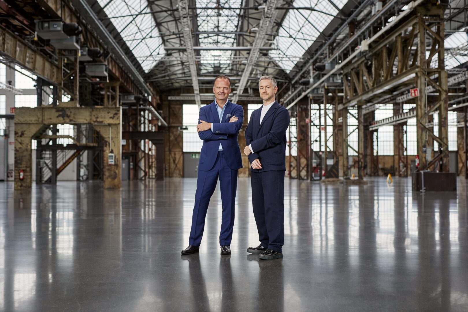 Man sieht zwei Männer in Anzügen, Walther Gehlen und Gilles Neiens, in einer alten Industriehalle auf dem Areal Böhler stehen, wo die Art Düsseldorf stattfindet.