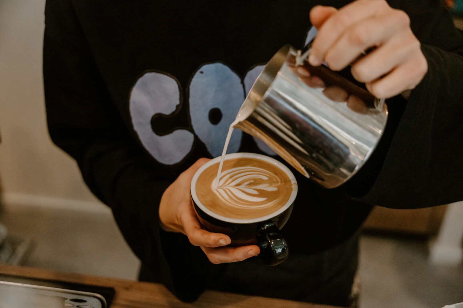 Man sieht, wie jemand jemand den Schaum auf den Cappuccino kunstvoll gießt.