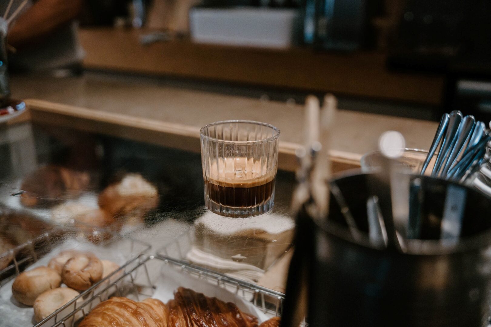 Man sieht die Kaffeetheke der Rösterei RVTC. Auf der Theke steht ein Espresso im geriffelten Glas, außerdem sieht man etwas Besteck und Gebäck im Anschnitt.