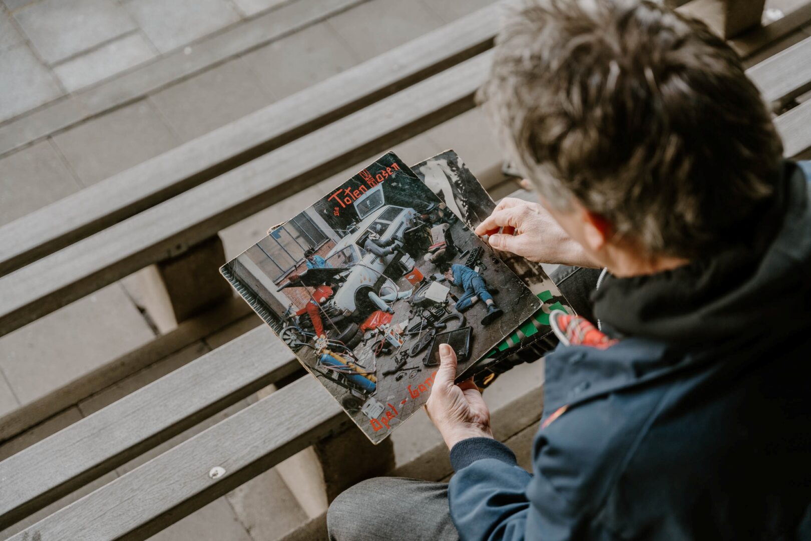 Schulterblick über die Schulter eines Mannes,d er auf einer Bank sitzt und das Album "Opel-Gang" der Toten Hosen in den Händen hält.