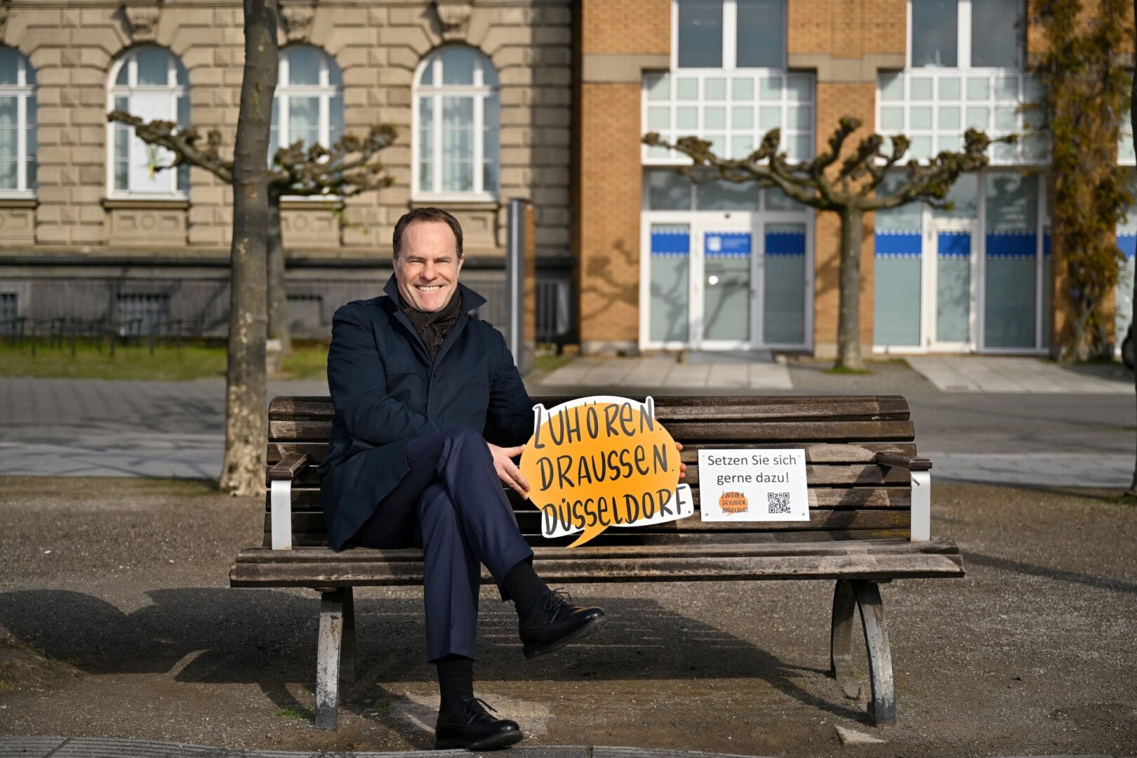 Oberbürgermeister Keller sitzt auf der "Zuhör.Bank" am Rathausufer.